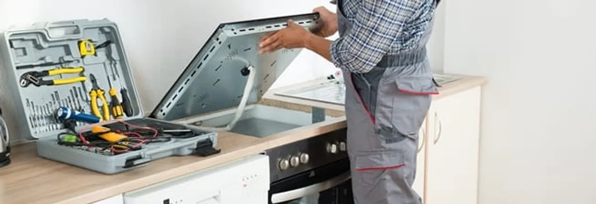 Cooktop repair technician lifting a built-in stovetop for service in Eugene, OR