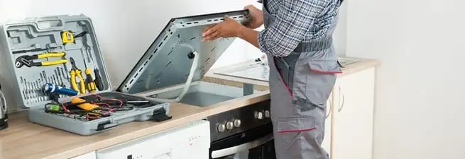 Cooktop repair technician lifting a built-in stovetop for service in Eugene, OR