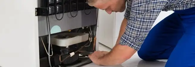 Refrigerator repair technician servicing the compressor and condenser area in Eugene, OR