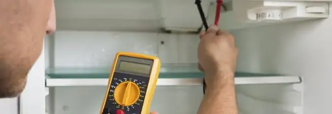 Refrigerator repair technician testing electrical components with a multimeter in Eugene, OR