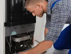 Refrigerator repair technician servicing the compressor and condenser area in Eugene, OR